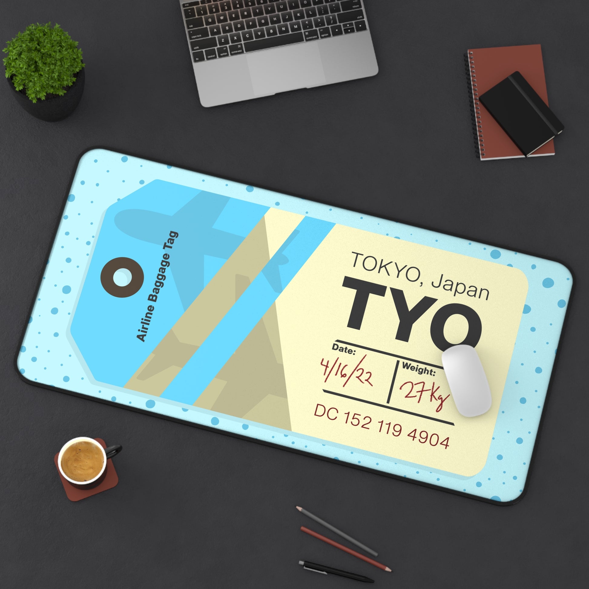A 31" x 15.5" desk mat with a dotted blue background and a blue and yellow Tokyo airline baggage tag on it sitting at an angle.