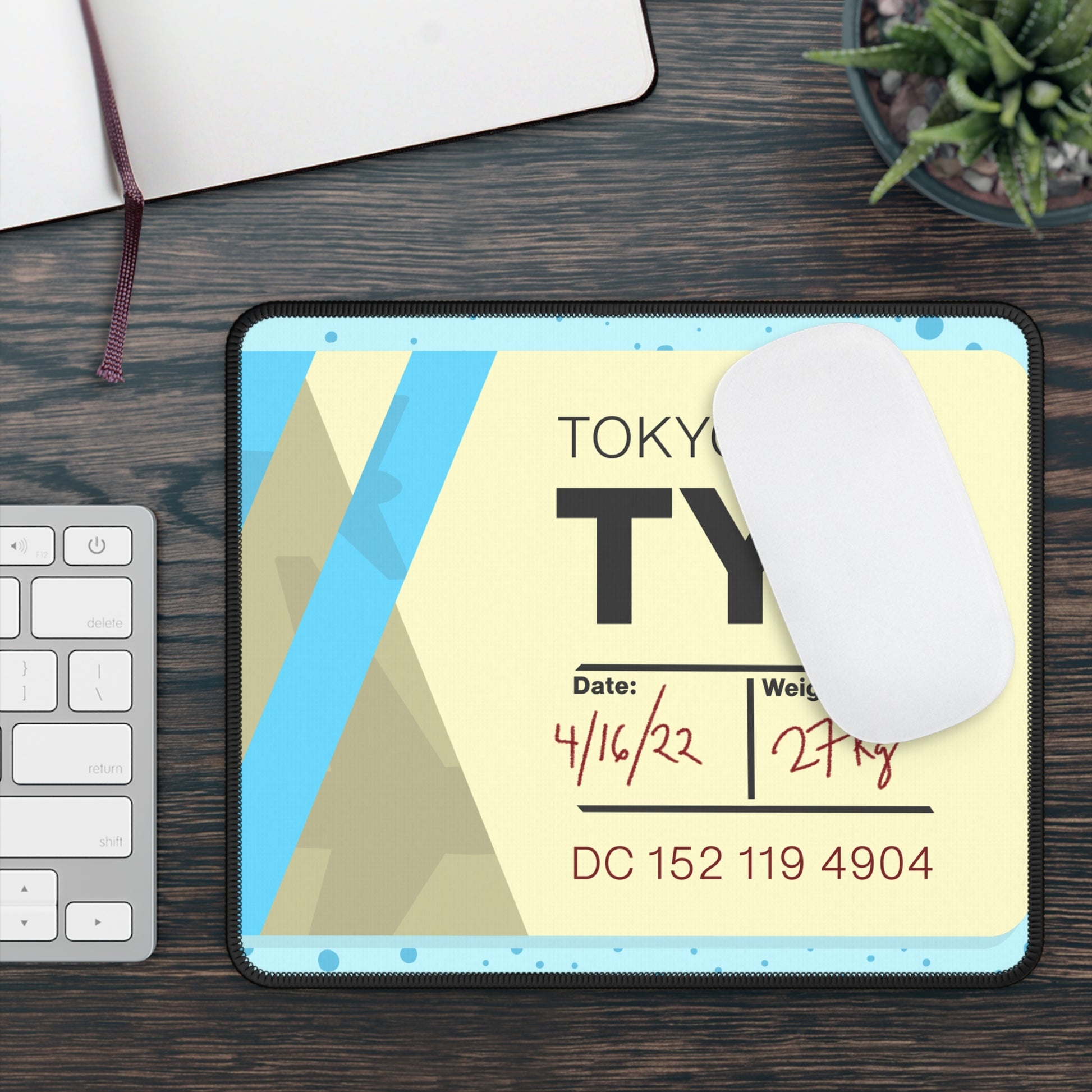A gaming mouse pad with a dotted blue background and a blue and yellow Tokyo airline baggage tag on it. A mouse sits on top of it.