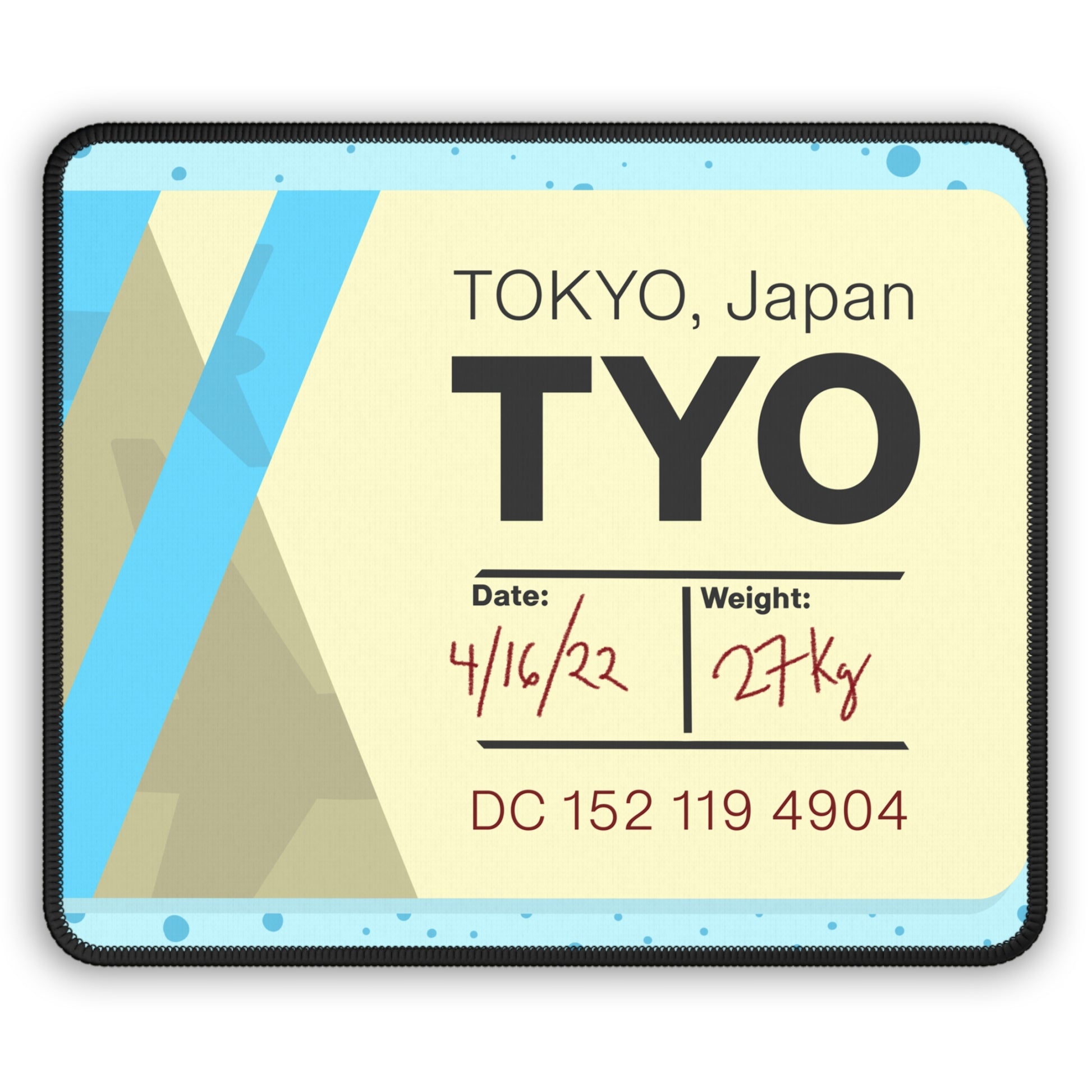 A gaming mouse pad with a dotted blue background and a blue and yellow Tokyo airline baggage tag on it.