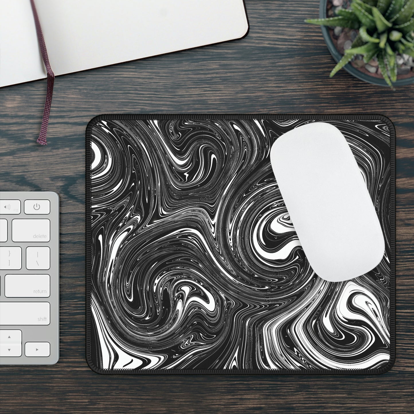 A gaming mouse pad with black and white swirls. A mouse sits on top of it.