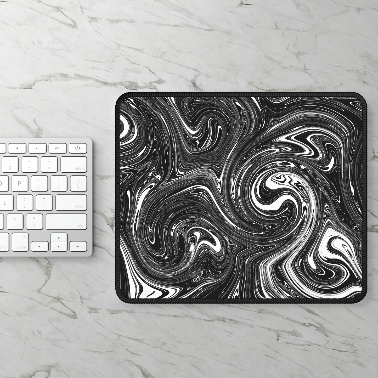 A gaming mouse pad with black and white swirls sitting next to a keyboard.