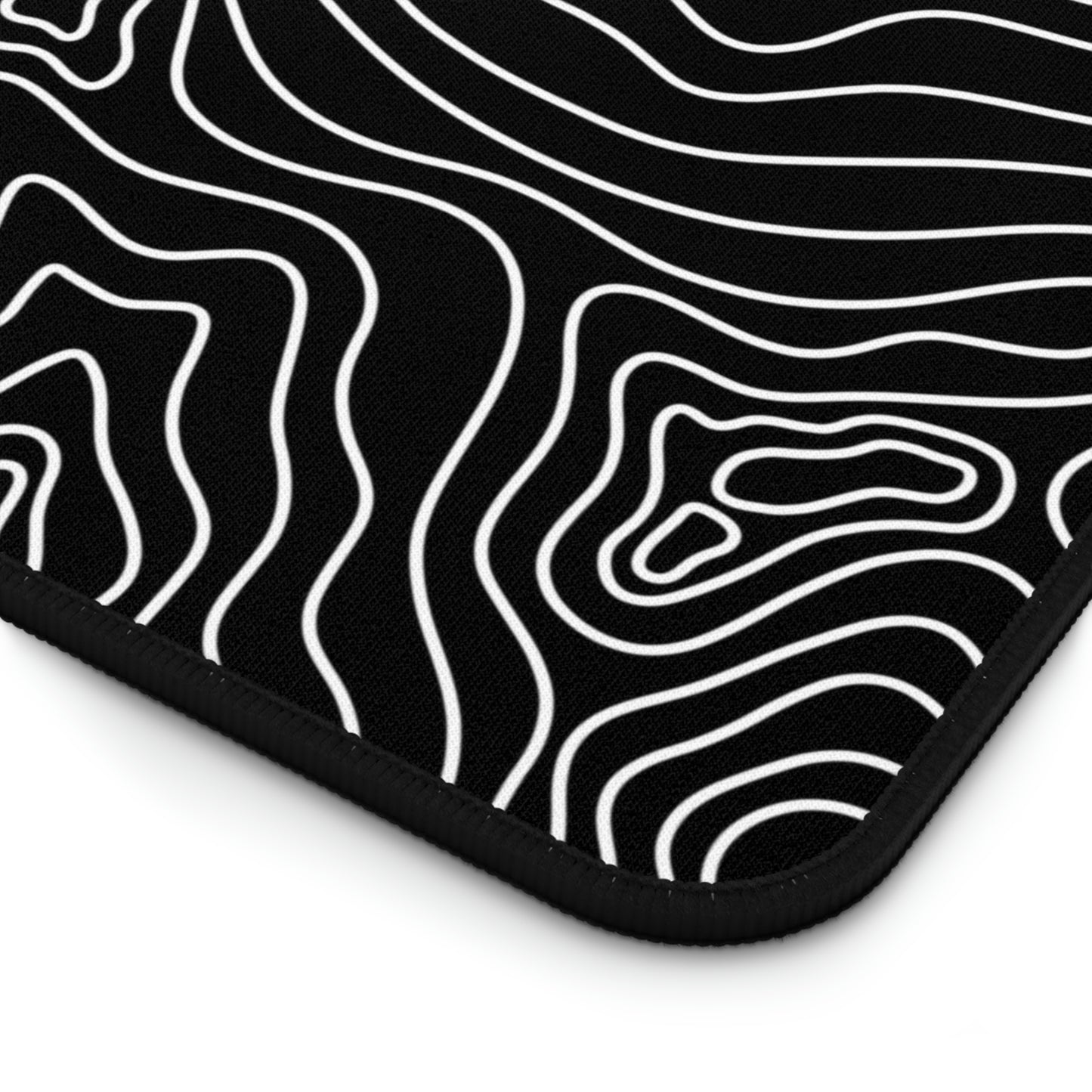 The bottom right corner of a 12" x 22" black desk mat with white topographic lines.