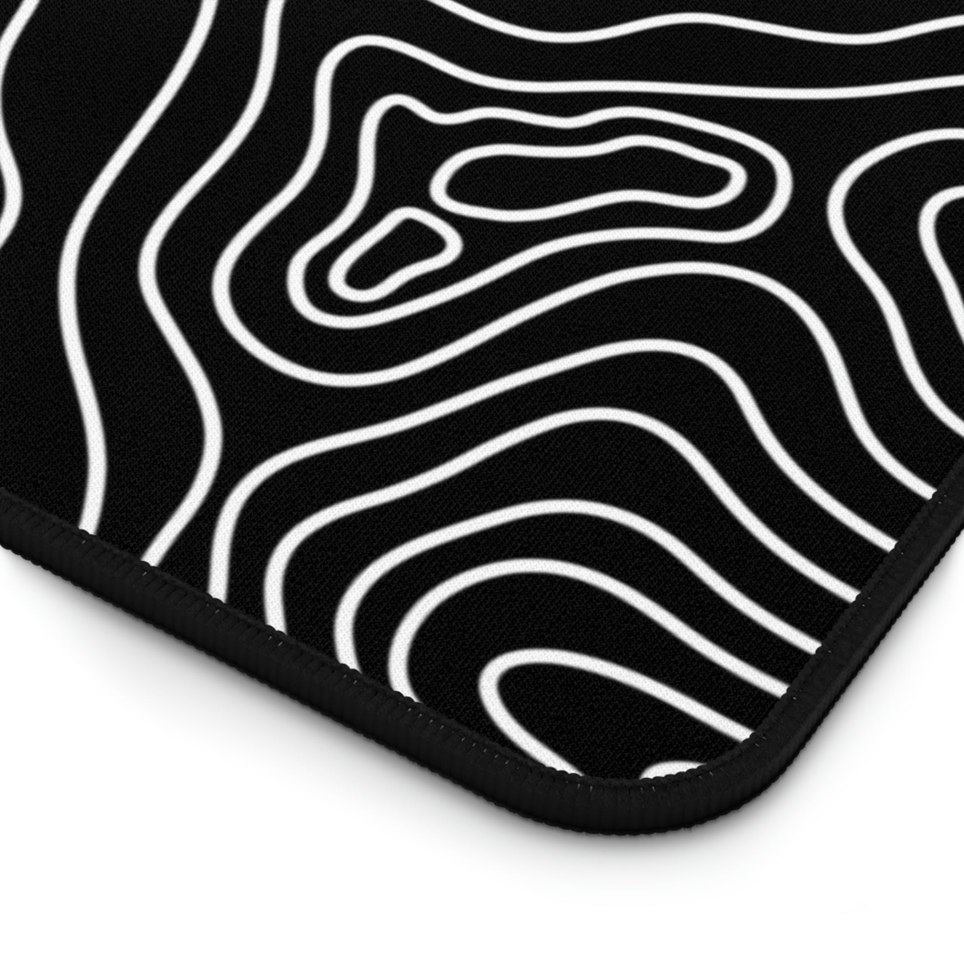 The bottom right corner of a 31" x 15.5" black desk mat with white topographic lines.