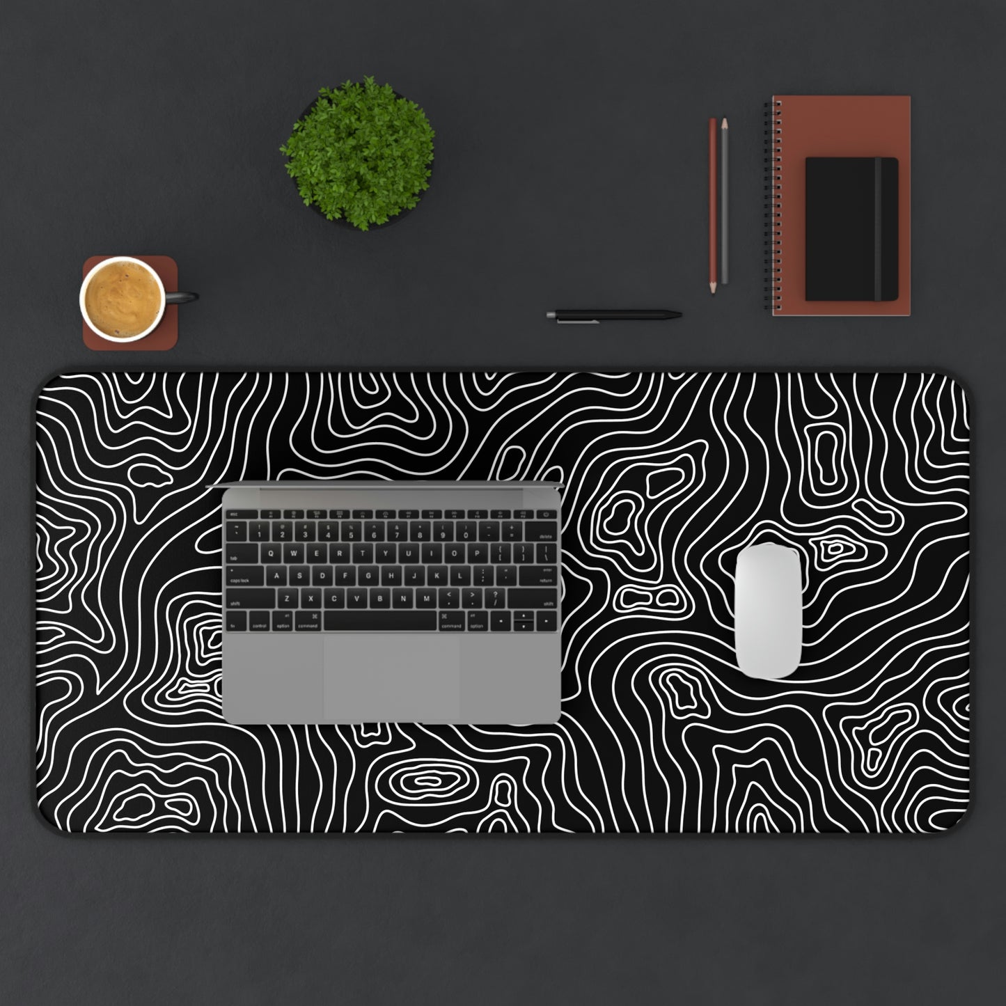 A 31" x 15.5" black desk mat with white topographic lines. A laptop and mouse sit on top of it.