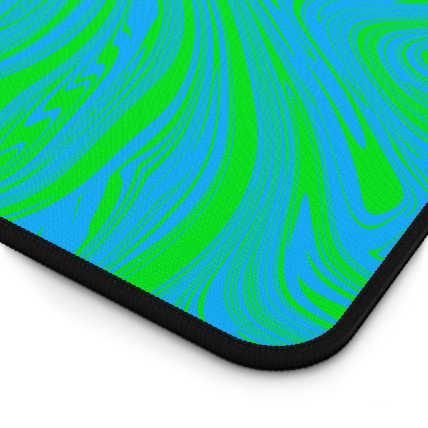 The corner of a 12" x 18" desk mat with blue and green swirls.