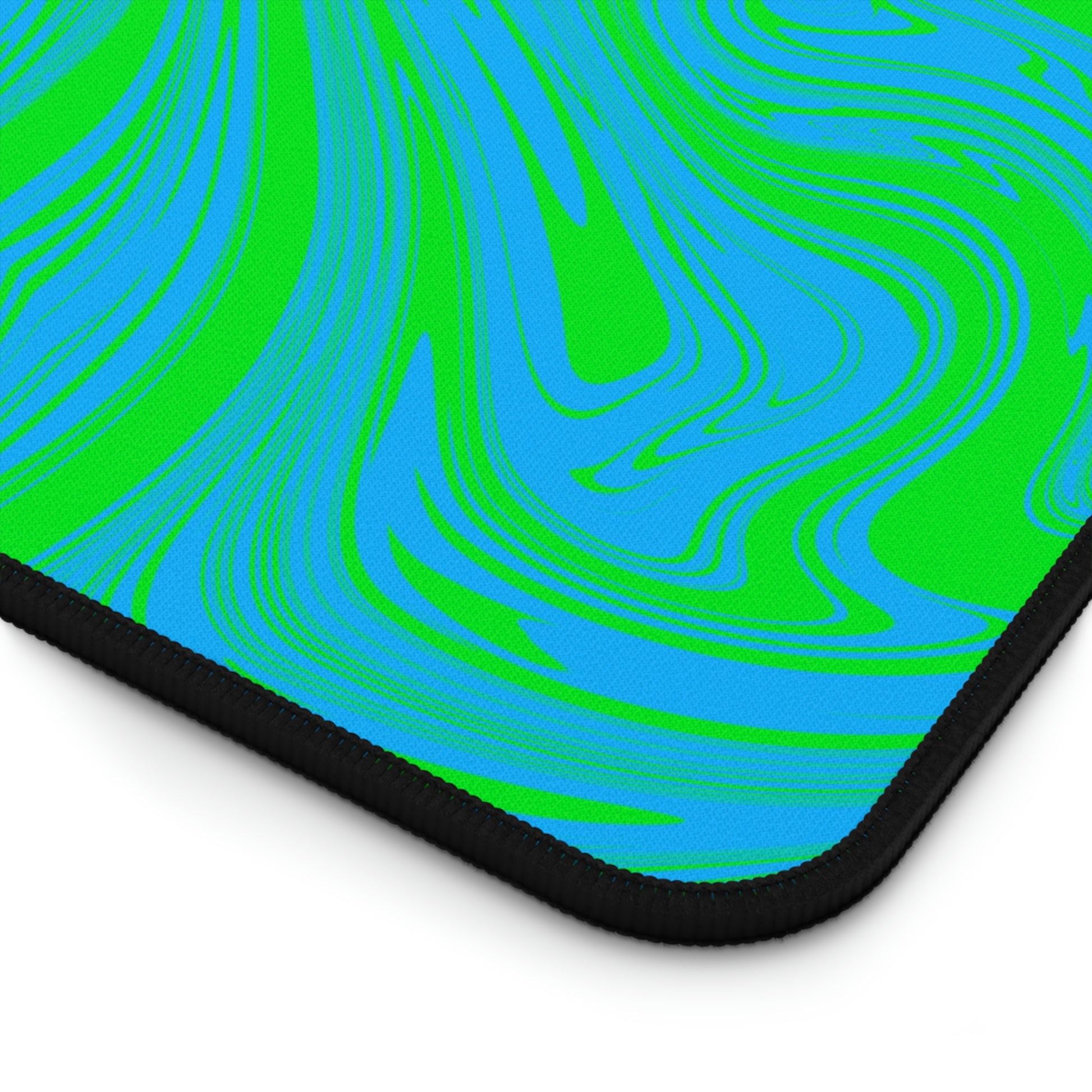 The corner of a 12" x 22" desk mat with blue and green swirls.
