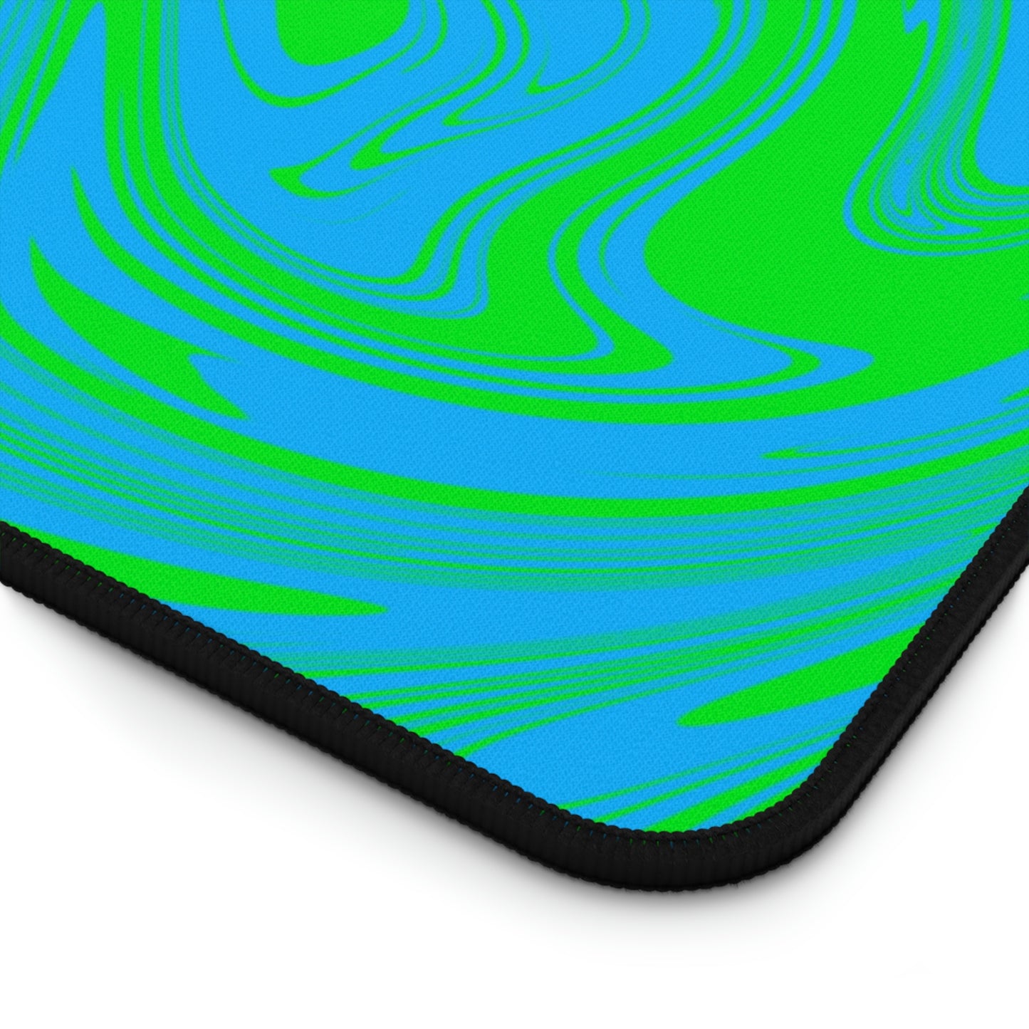 The corner of a 31" x 15.5" desk mat with blue and green swirls.