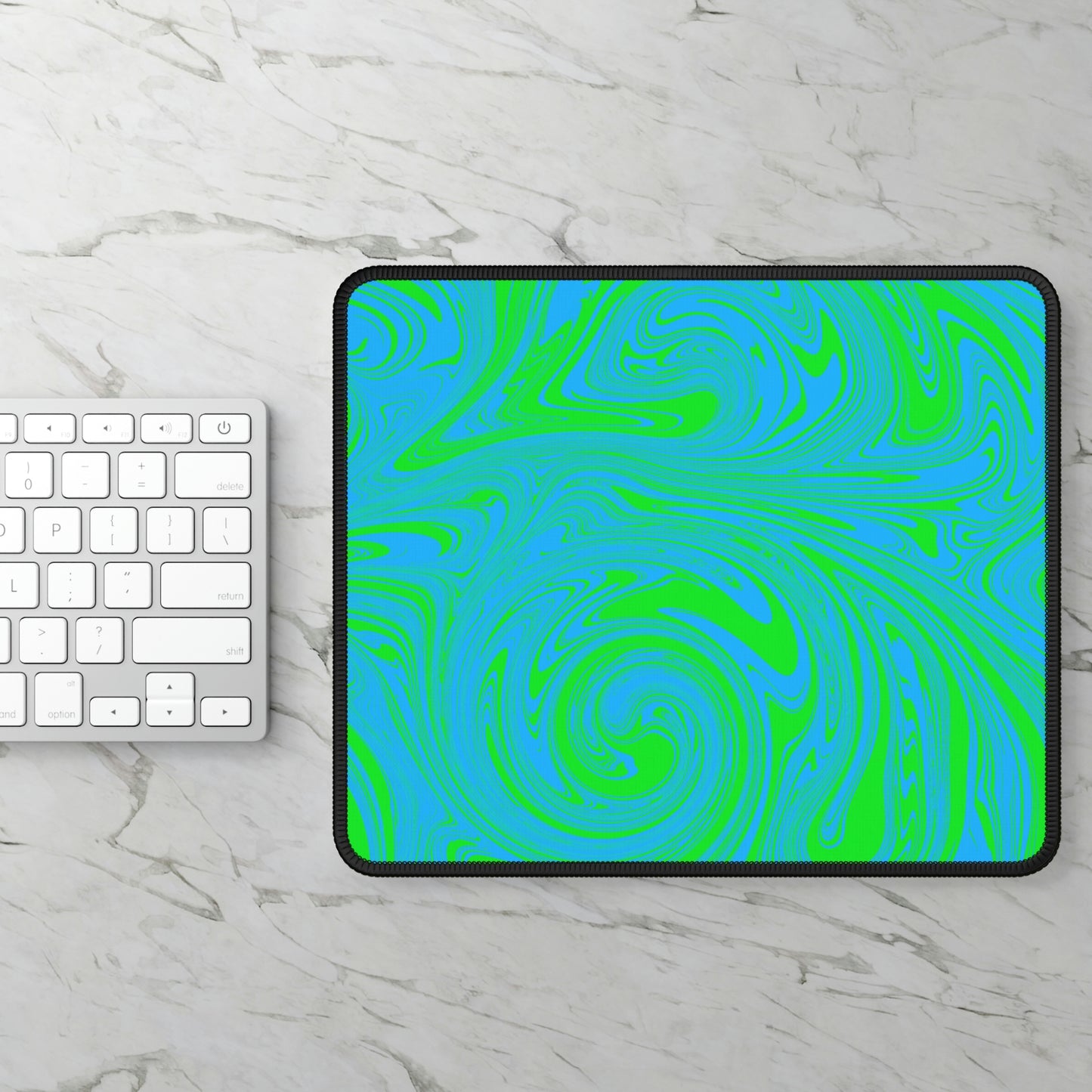 A gaming mouse pad with blue and green swirls sitting next to a keyboard.