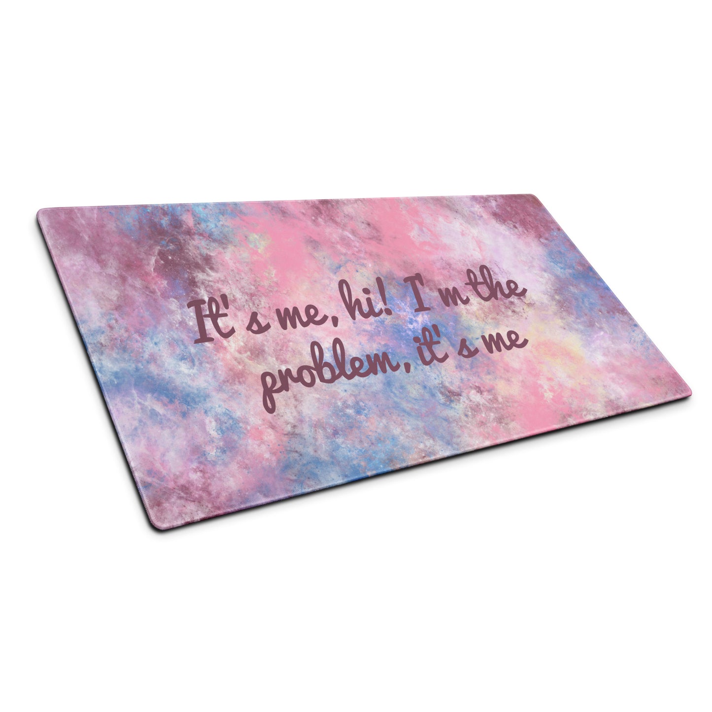 A pink, blue, and white gaming desk pad with the quote It's me, hi! I'm the problem, it's me. The desk pad sits at an angle.