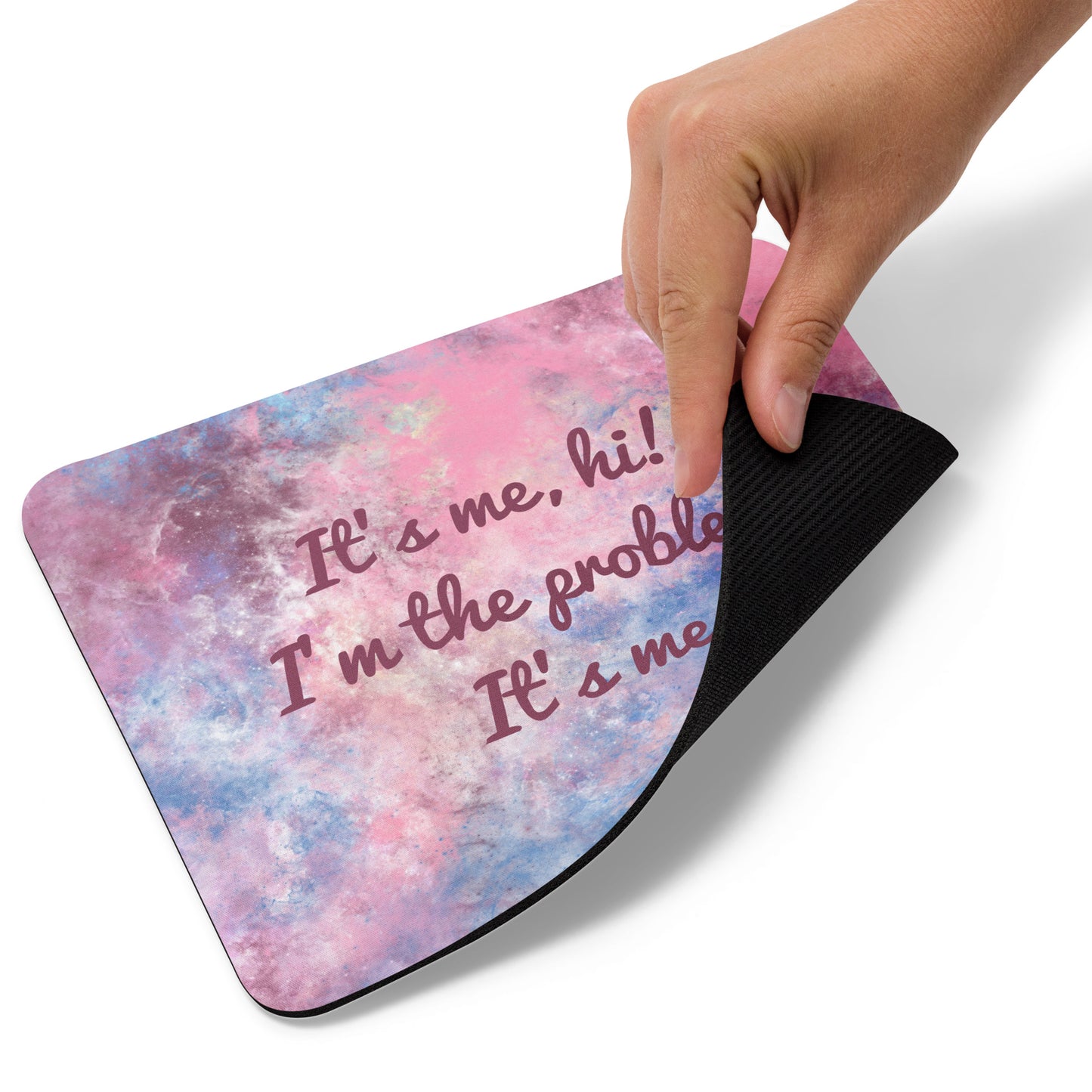A blue, pink, and white mouse pad with the quote It's me, hi! I'm the problem, it's me. The bottom right corner of the mouse pad is lifted up.