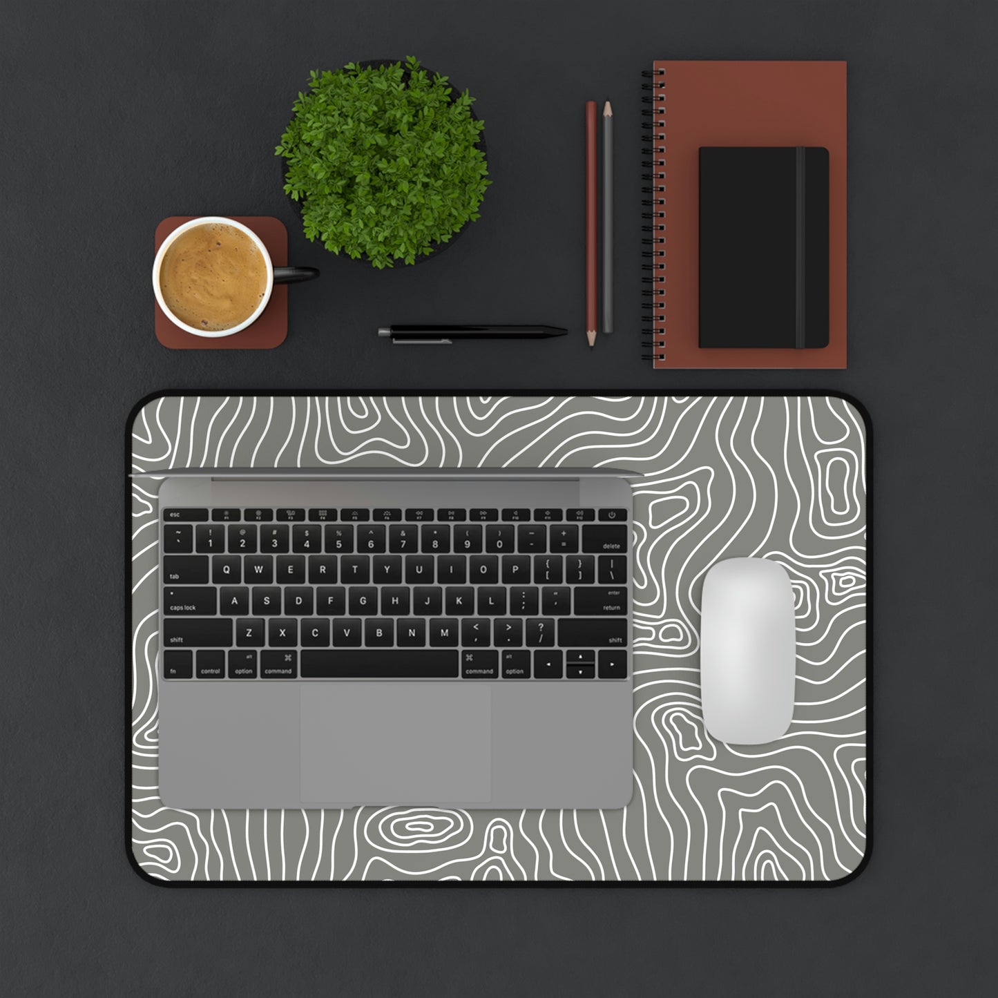 A 12" x 18" gray desk mat with white topographic lines. A laptop and mouse sit on top of it.