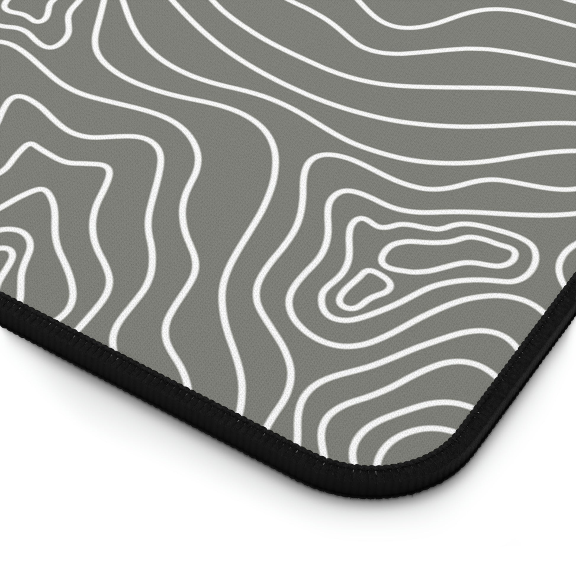 The bottom right corner of a 12" x 22" gray desk mat with white topographic lines.