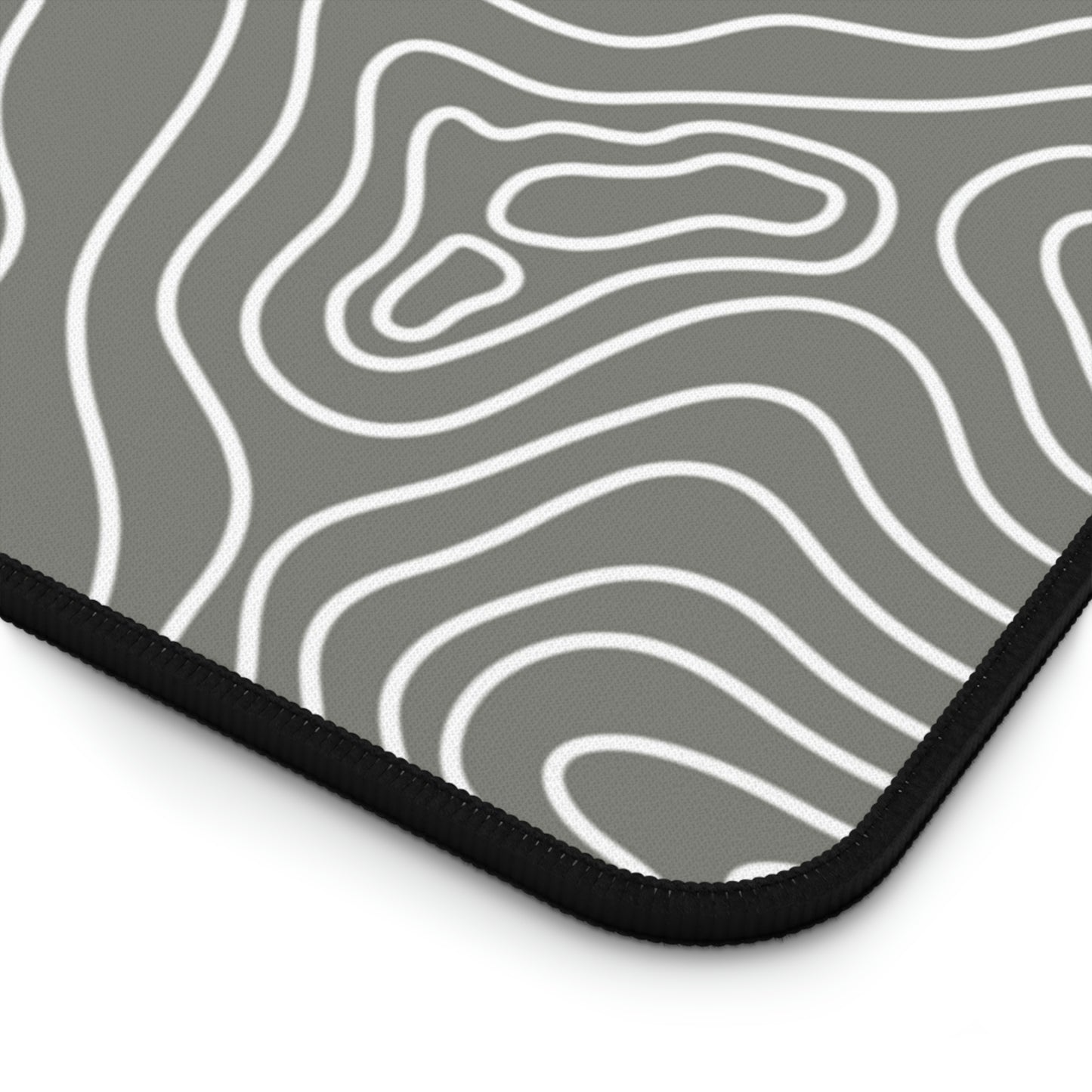 The bottom right corner of a 31" x 15.5" gray desk mat with white topographic lines.