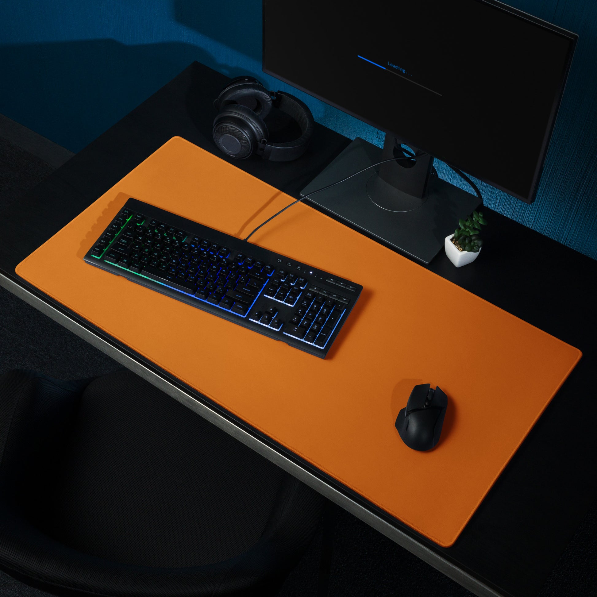 A 36" x 18" orange gaming desk pad sitting on a black desk with a monitor, keyboard, and mouse.