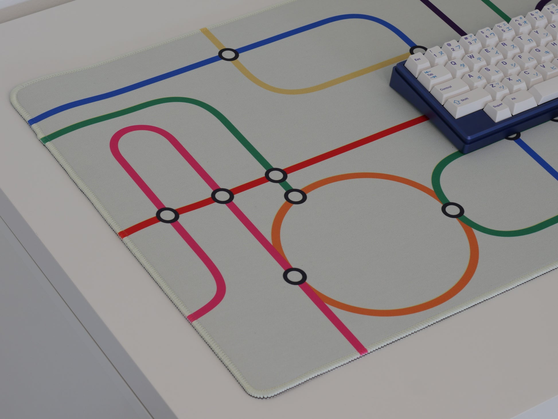 The left side of the subway transit desk mat. The desk mat has a white background and colorful lines.