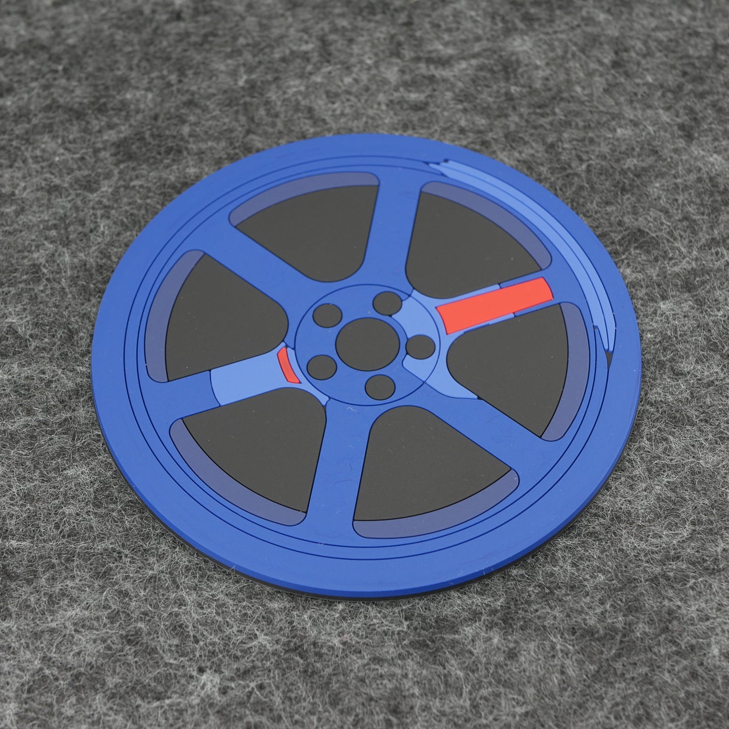 A blue TE wheel PVC rubber coaster sitting on a gray desk mat.