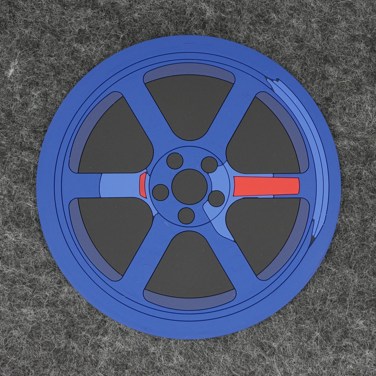 The top of a blue TE wheel PVC rubber coaster sitting on a gray desk mat.