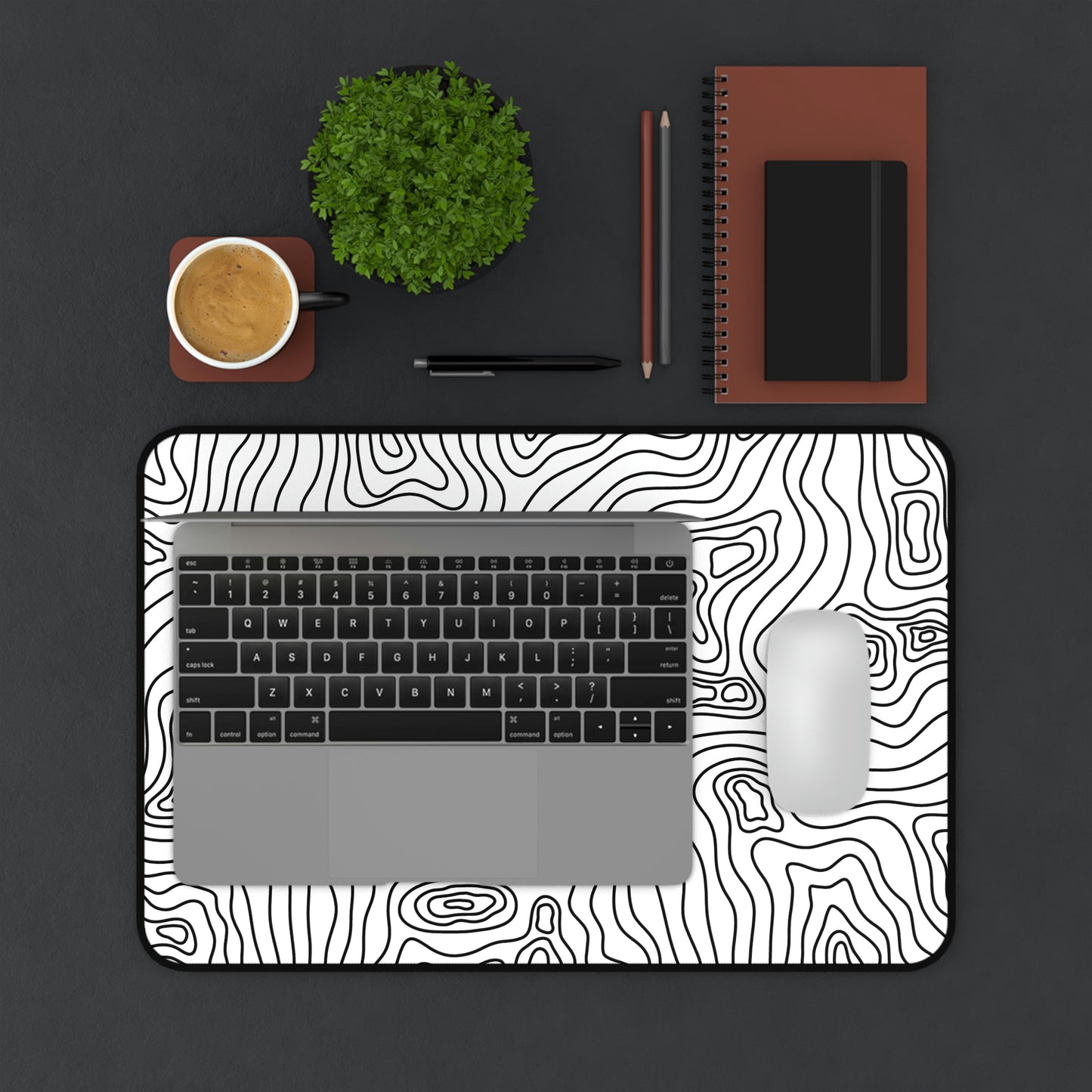 A 12" x 18" white desk mat with black topographic lines. A laptop and mouse sit on top of it.