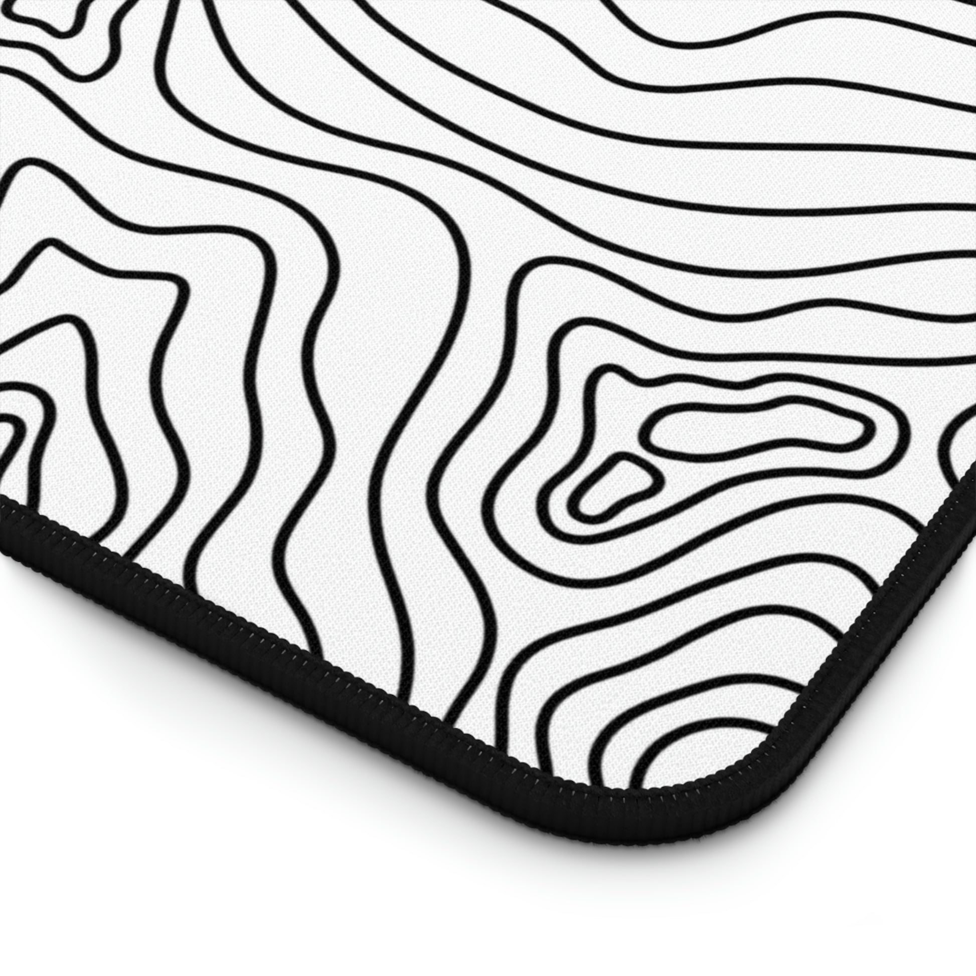 The bottom right corner of a 12" x 22" white desk mat with black topographic lines.