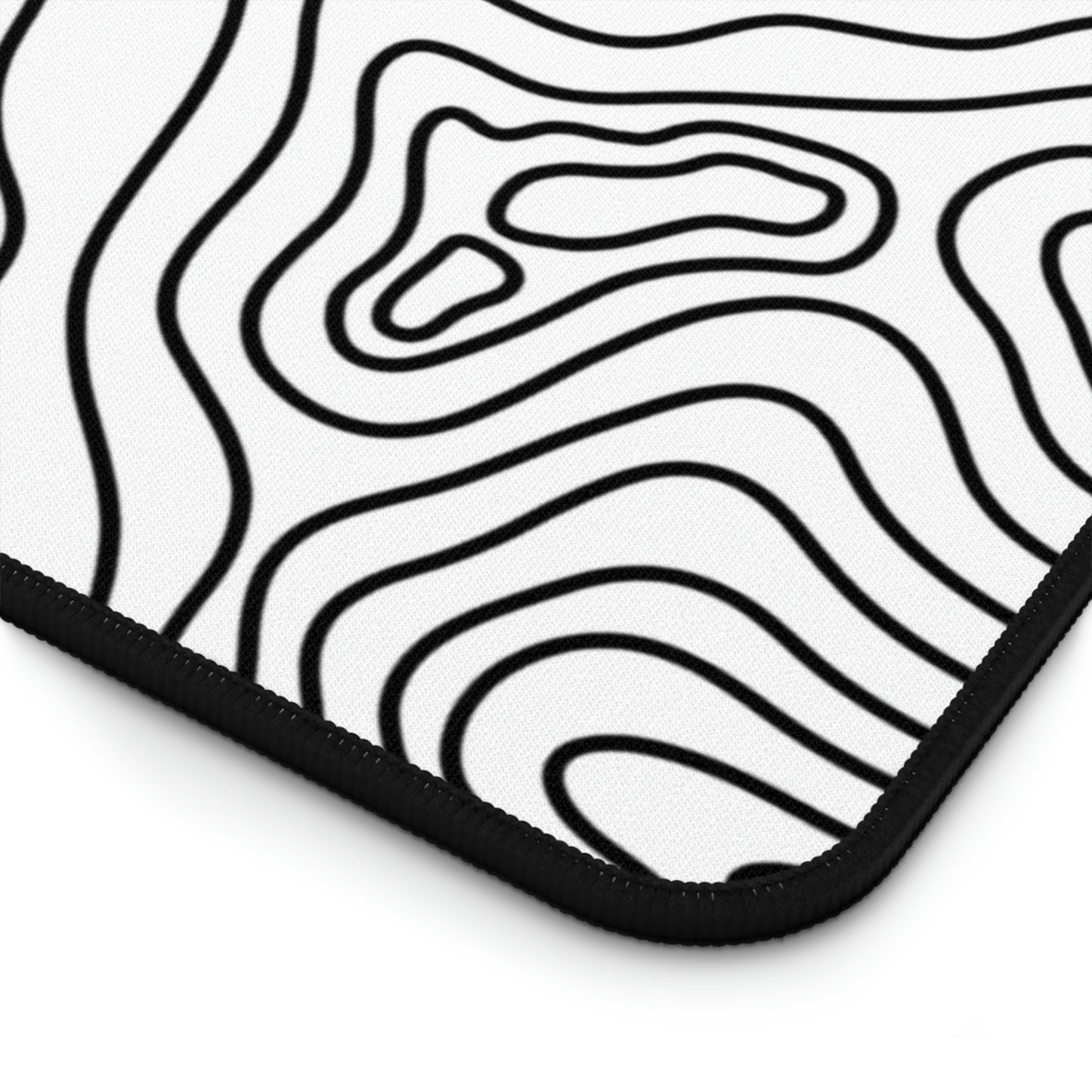 The bottom right corner of a 31" x 15.5" white topographic desk mat. The desk mat is white with black topographic lines.